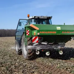Ciągnik AMAZONE rozsypuje nawóz na polu.