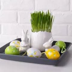 Wielkanocna dekoracja: owies, pisanki i zające na szarej tacy.