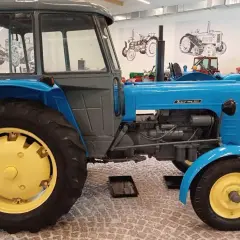 Niebieski Zetor 3011 z żółtymi felgami, stojący w muzeum obok innych zabytkowych traktorów.