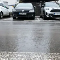 Trzy samochody zaparkowane na mokrym, błyszczącym od lodu asfalcie.
