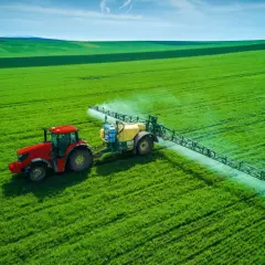Czerwony traktor z opryskiwaczem na zielonym polu, rozpyla nawóz, by zapewnić roślinom saletrę.