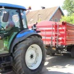 B+E: Niebieski traktor z przyczepą jedzie po drodze.