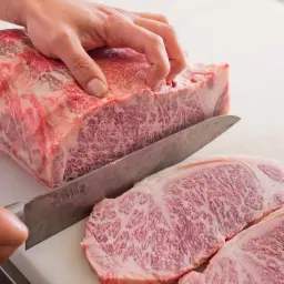 Ręka kroi luksusowe mięso wagyu na desce. Widoczne marmurkowe przerosty tłuszczu świadczą o jego wyjątkowej jakości.