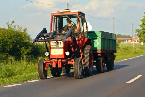 Czerwony traktor z przyczepą jedzie drogą. Zastanawiasz się, ile kosztuje przegląd ciągnika rolniczego?