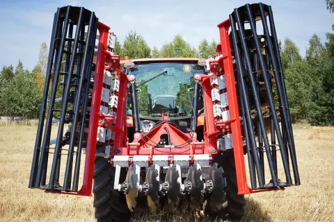 Czerwony traktor z zamontowanym agregatem do bronowania, gotowy do pracy na polu.