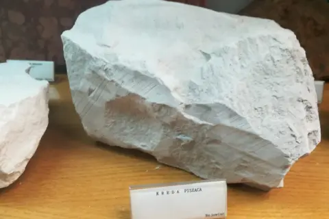 Duży blok białej, porowatej skały, prawdopodobnie kreda nawozowa, z widocznymi śladami obróbki.
