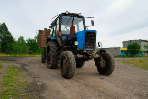 Niebieski traktor z przyczepą pełną siana, gotowy do pracy. Traktorzysta pewnie zaraz ruszy w pole.