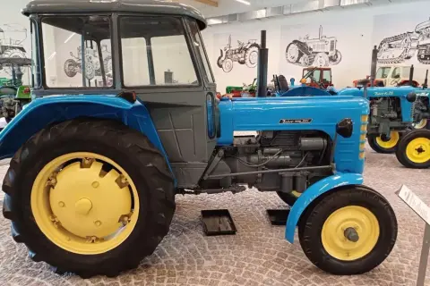 Niebieski Zetor 3011 z żółtymi felgami, stojący w muzeum obok innych zabytkowych traktorów.