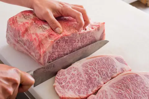 Ręka kroi luksusowe mięso wagyu na desce. Widoczne marmurkowe przerosty tłuszczu świadczą o jego wyjątkowej jakości.