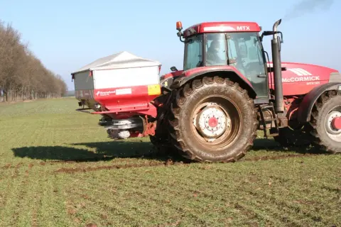 Czerwony traktor McCormick MTX 185 z rozsiewaczem nawozów, który właśnie rozprowadza **nitrabor** na polu.