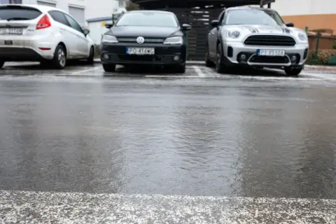 Trzy samochody zaparkowane na mokrym, błyszczącym od lodu asfalcie.