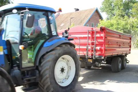 B+E: Niebieski traktor z przyczepą jedzie po drodze.