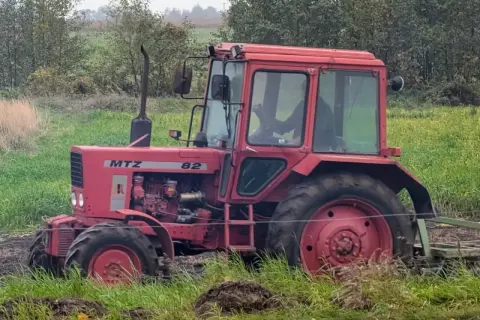 Czerwony ciągnik Belarus 820 pracuje na polu, za nim widać las i zielone pola.