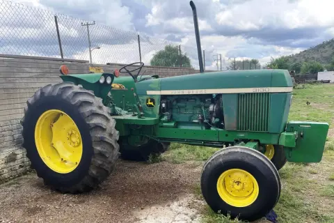 Zielony traktor John Deere 3130 z żółtymi felgami stoi na żwirowym podwórzu, gotowy do pracy na polu.