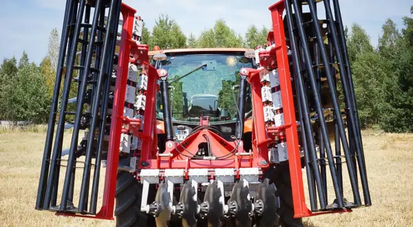 Czerwony traktor z zamontowanym agregatem do bronowania, gotowy do pracy na polu.