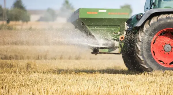 Traktor rozsiewa wapno magnezowe na polu. Drobinki nawozu unoszą się w powietrzu, poprawiając jakość gleby.