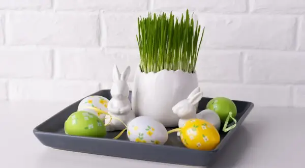 Wielkanocna dekoracja: owies, pisanki i zające na szarej tacy.