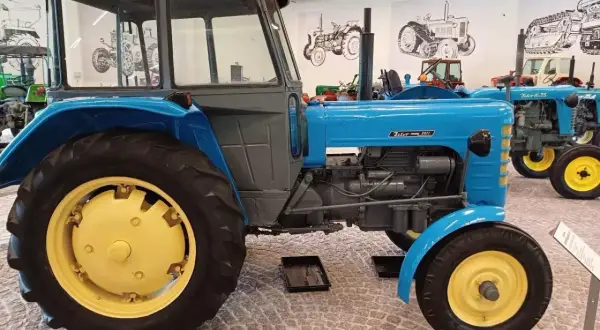 Niebieski Zetor 3011 z żółtymi felgami, stojący w muzeum obok innych zabytkowych traktorów.