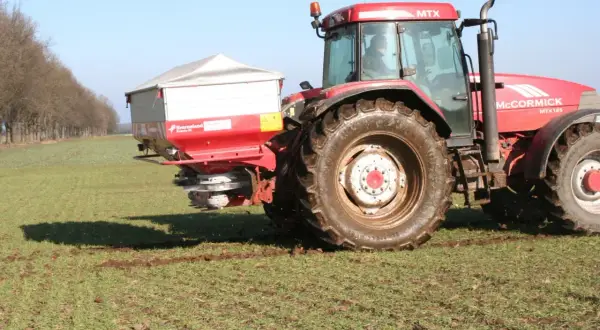 Czerwony traktor McCormick MTX 185 z rozsiewaczem nawozów, który właśnie rozprowadza **nitrabor** na polu.