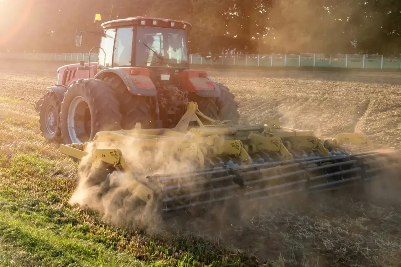 Czerwony traktor z glebogryzarką spulchnia ziemię, przygotowując pole do siewu. To pokazuje, do czego służy glebogryzarka.