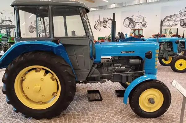 Niebieski Zetor 3011 z żółtymi felgami, stojący w muzeum obok innych zabytkowych traktorów.