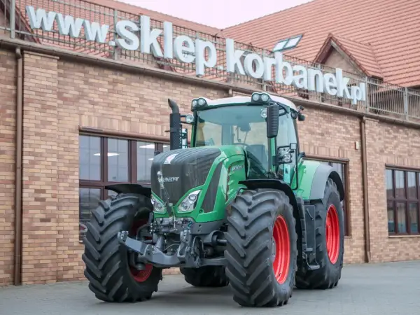 Potężny zielony traktor Fendt 936 z czerwonymi felgami stoi przed budynkiem sklepu.