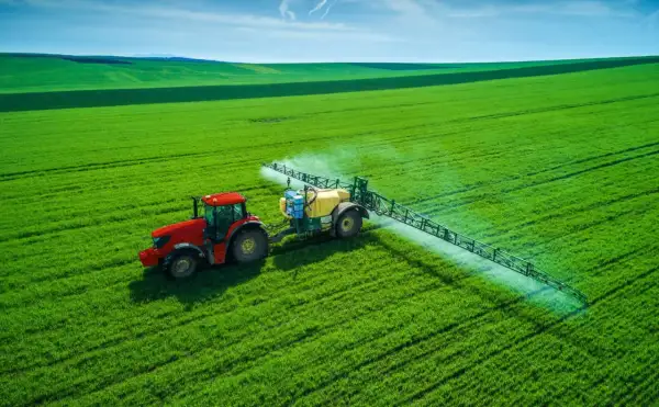 Czerwony traktor z opryskiwaczem na zielonym polu, rozpyla nawóz, by zapewnić roślinom saletrę.