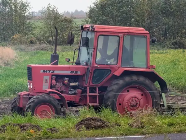 Czerwony ciągnik Belarus 820 pracuje na polu, za nim widać las i zielone pola.